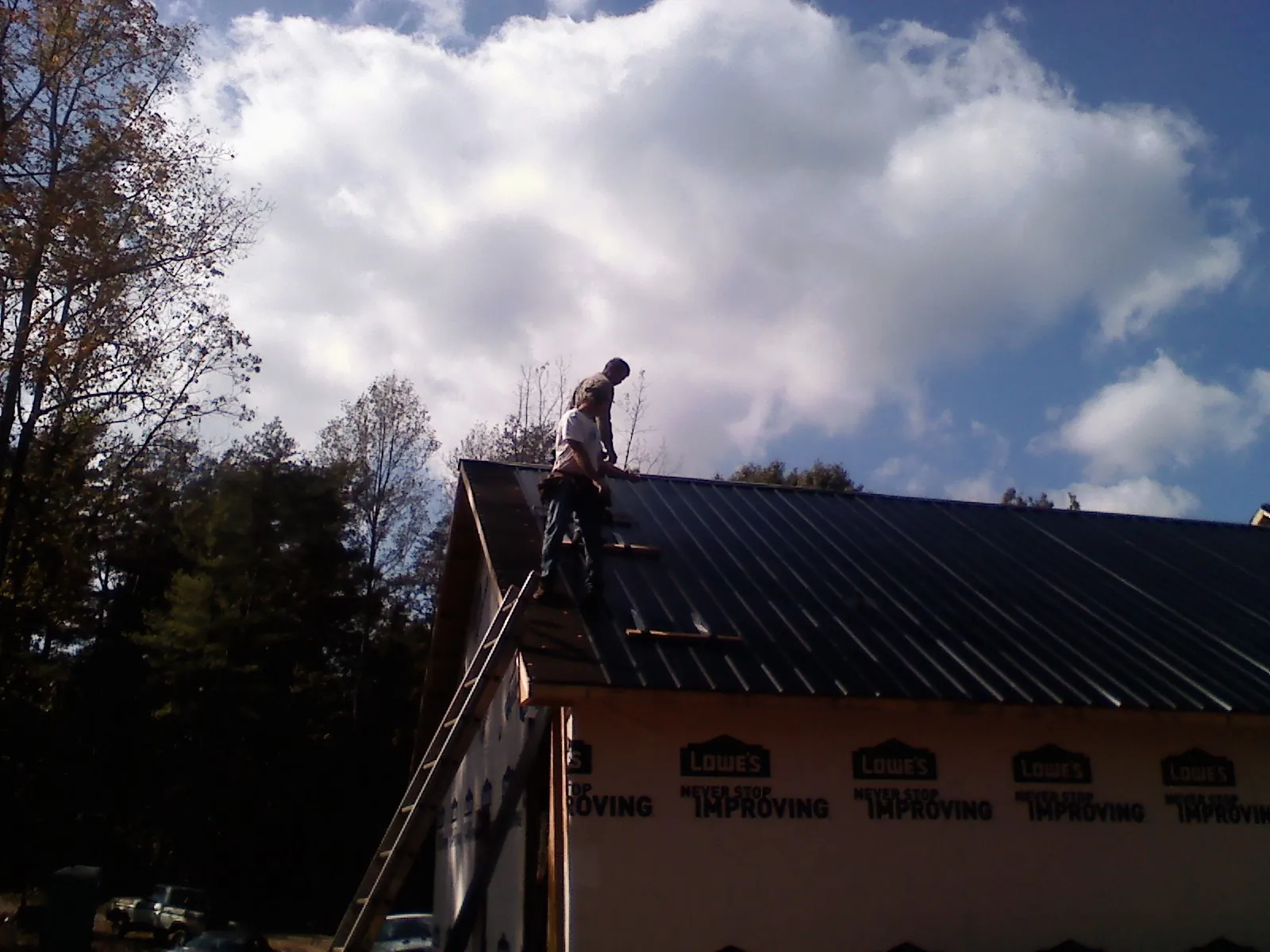 Roofer fastening dark metal panels high against a cloudy sky, from a Roof Inspection job in Harrisville