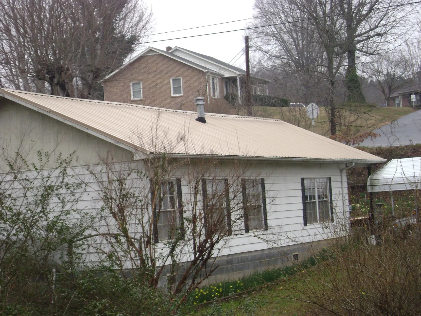 Tan metal roof on a white sided house set into a hillside — Commercial Roofing by Roofing Brothers in Harrisville